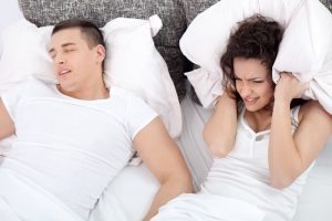 Woman Covers Her Ears with a Pillow Whild Husband Snores